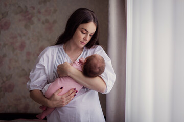 A young mother rocks her kid and sings a lullaby at home. A restless Child does not sleep. Caring for newborn motherhood. Mother's love. Nanny. Tired woman. Rest sleep insomnia. mom holds baby in arms