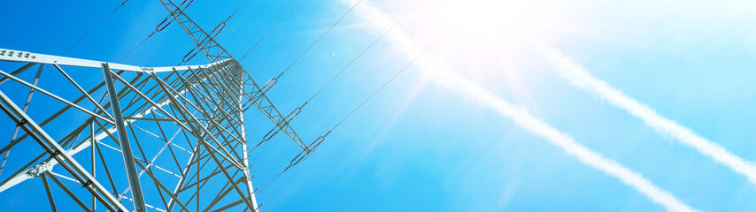 Electricity background banner panorama - Voltage power lines / high voltage electric transmission tower with blue sky and shining sun