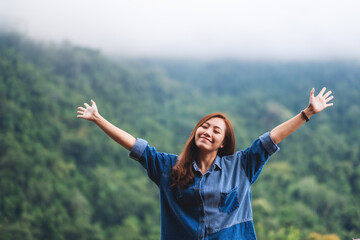 A female traveler close her eyes and open arms with a beautiful green mountains on foggy day in background