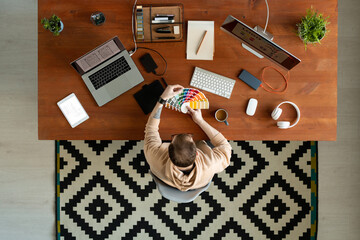 Wall Mural - Above view of busy UI designer with tattoo sitting at table with devices and watching color palette