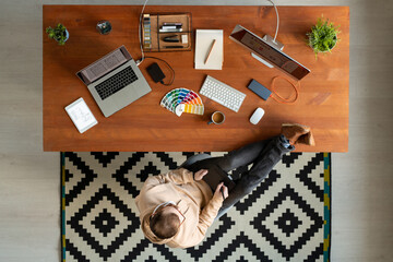 Wall Mural - Directly above view of young man keeping feet on table and using drawing pad while working on graphic design