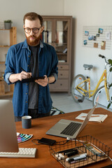 Wall Mural - Focused creative young graphic designer with beard standing at table and looking at computer monitor while working with digitizer