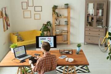 Wall Mural - Rear view of busy brand designer in checkered shirt sitting at desk in home office and editing font using digitizer tablet