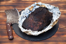 Beef Brisket In Foil. Ax For Meat On A Wooden Table Near The Meat