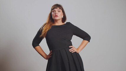 Plus size elegant model with stylish hairstyle in black dress posing at grey background in studio isolated