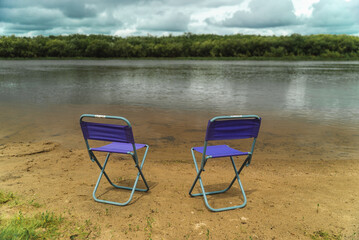 Two chairs by the river. A place of relaxation in nature. Summer rest