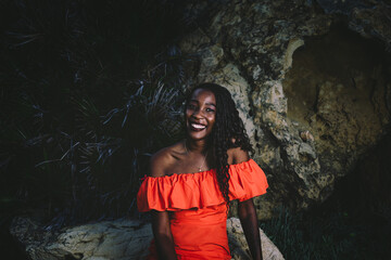 An elegant and beautiful young black woman in a red dress in a shore background in summer. 