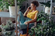 © likoper - Young woman using mobile phone. Young florist in eyeglasses sitting on armchair and using mobile phone in the room with plants.