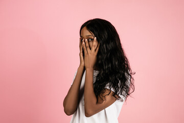 Wall Mural - Scared. Cheerful african-american young woman isolated on pink background, emotional and expressive. Concept of human emotions, facial expression, sales, ad. Beautiful model with long curly hair.