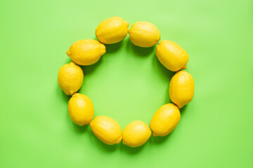 top view of ripe yellow lemons arranged in round empty frame on green background