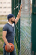 © Vladimir - Man with a basketball looks out from behind a fence on the street during the day
