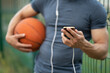 © Vladimir - Man holds a basketball in his hand, looks at a smartphone and listens to music with headphones on the street close up