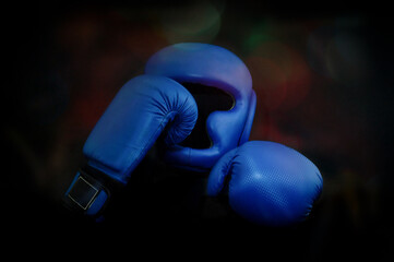 Two blue Boxing gloves and a protective helmet on a black background with rainbow highlights.