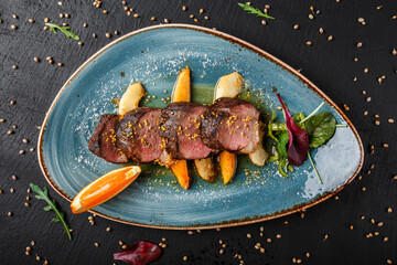 Wall Mural - Juicy duck breast steaks with caramelized fruit, mango, apple and sauce of orange on plate over dark stone background. Hot Meat Dishes. Top view