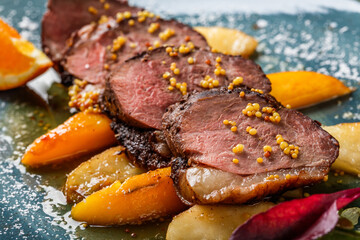 Wall Mural - Juicy duck breast steaks with caramelized fruit, mango, apple and sauce of orange on plate over dark stone background. Hot Meat Dishes