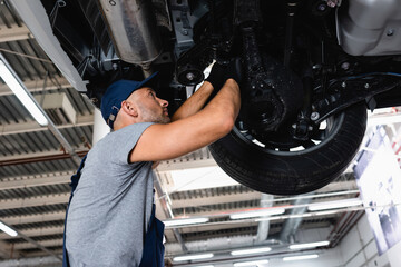 low angle view of technician in cap repairing car in service station