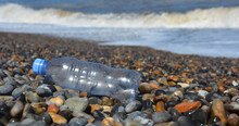 Close Up Of Discarded Plastic Drinks Bottle Washed Up On Pebble Beach By Waves