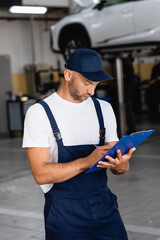 Wall Mural - handsome mechanic in uniform and cap writing while holding clipboard