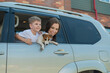 Beautiful caucasian woman travels with a child and a dog. Mom and son leaned out of the car window in an embrace with a puppy of Jack Russell Terrier. Happy family go on a car trip.