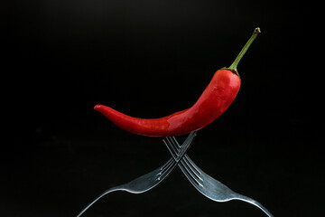 red chili peppers lie on two crossed forks on a dark background.