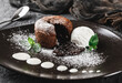 Mini chocolate cake or fondant with chocolate icing, ice cream, and mint leaves on a plate, dark background, close up. Delecious sweets and dessert