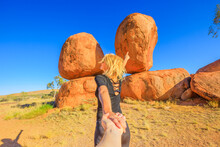 Hand In Hand Couple At Devils Marbles, Northern Territory: The Eggs Of Mythical Rainbow Serpent. Follow Me, Tourist Woman At Iconic Landscape Of Outback, One Of Australia's Most Famous Natural Wonders