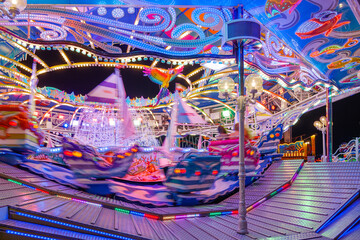 Selected focus and night scenery at illuminating amusement ride of carousel with speedy movement of rotating sloping platform with long exposure technique at Rheinkirmes in Düsseldorf, Germany. 