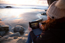 Woman On The Beach Looking At Sunset Through Ipad Screen