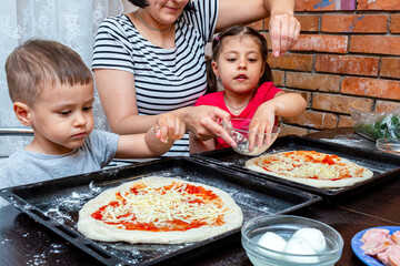 little boy and girl helping mom make pizza at home