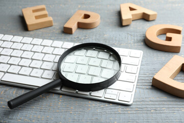 Magnifier glass, keyboard and letters on light grey wooden table, closeup. Find keywords concept