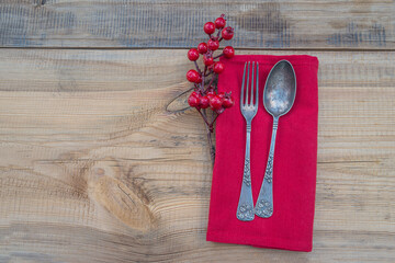 Wall Mural - Festive table setting for christmas dinner. Vintage fork and spoon, holly berries on red napkin and wooden non paint background. Space for text, flat lay