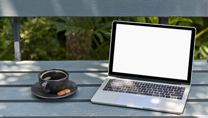 Close - up shot of Mockup laptop blank screen with coffee on a wooden chair in the garden.