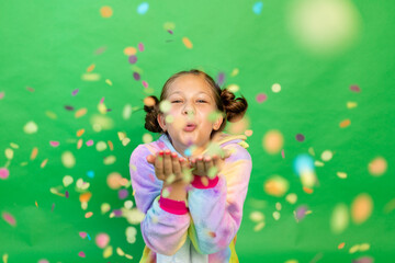 a little girl on a green isolated background in a bright suit blows away a streamer. Space for text. The concept of a holiday, Birthday and sales