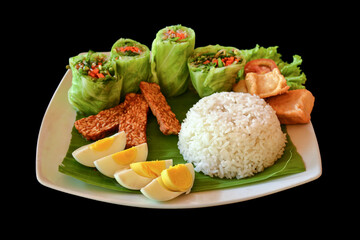 Traditional indonesian meal made of rice, vegetable spring rolls, fried tempeh and hard boiled eggs, isolated on black background.