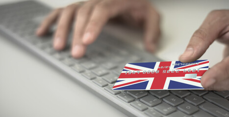 Man pays online with plastic bank card with printed flag of the United Kingdom. Fictional numbers