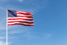 Beautiful American Flag Waving In The Wind, With Vibrant Red White And Blue Colors Against Blue Sky, With Copy Space.