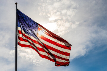 large american flag glowing from backlight from the sun, against cloudy sky