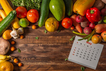 Frame Of Assorted Fresh Fruits And Vegetables And Calendar In English Language On Wooden Background