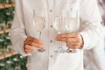 Faceless man wearing white shirt holding three champaagne glasses in his hands