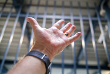 Man's Hand Against Bars As A Prison Incarceration Concept. 