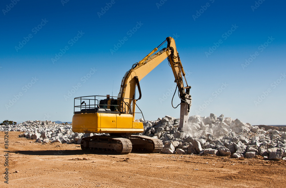 The breaker used to break up boulders in an open cast mine. Large yellow machinery crushing spodumene ore in a lithium mine.