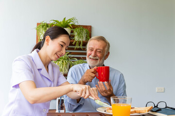 Asian nurse enjoy assist senior man having breakfast and happy together