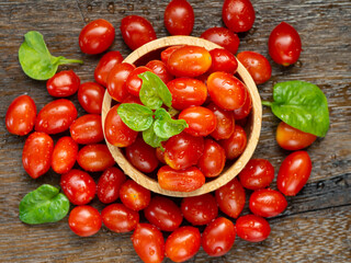 Small red fresh tomatos in wood bowl on wood table with nature light.