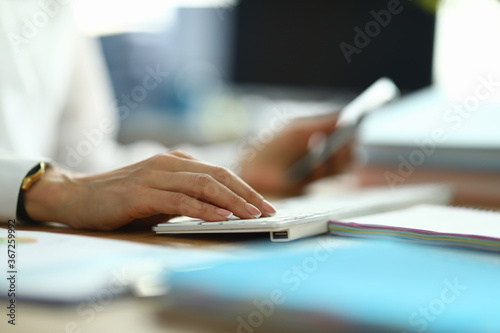 Nurse type text. Woman in white coat hold her hand on white keyboard. Doctor press button with her finger. On table are document, paper, form. Specialist serves population in workplace.