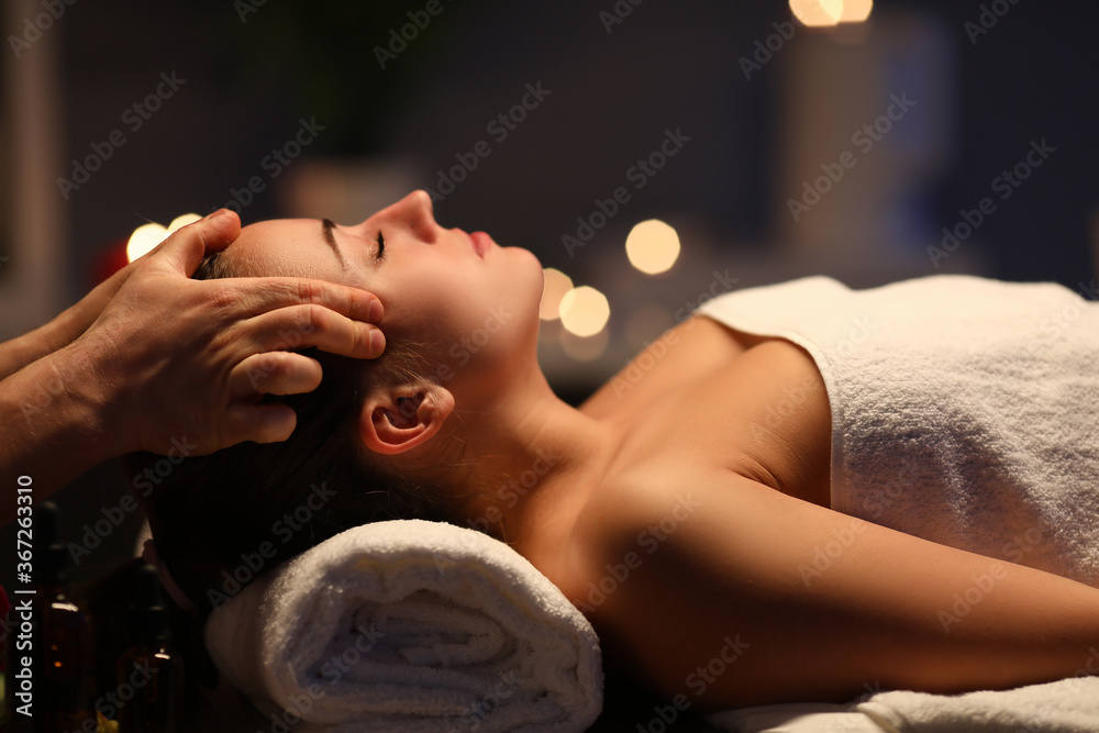 Woman lay on couch on her back with closed eyes and enjoy. Man make relaxing and therapeutic head massage at weight. Spa client has thrown her head back and rejuvenate. Wellness procedures in spa - obrazy, fototapety, plakaty 