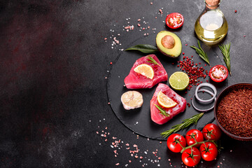 Fresh tuna fillet steaks with spices and herbs on a black background