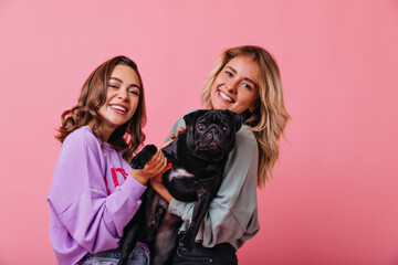 refined brown-haired girl posing with pleasure beside cute puppy. elegant blonde young woman holding