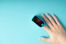 An essential medical device for hypoxia. Female finger in a pulse oximeter on a blue background with copyspace