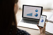 © fizkes - Close up back view of woman sit at desk working using laptop smartphone synchronize devices analyzing finances, female student studying on computer and cellphone gadget, distant education concept