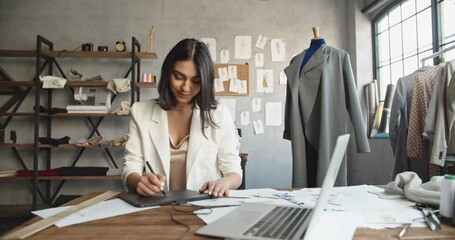 Wall Mural - Asian female clothing designer is drawing her sketches on graphics tablet, preparing her new collection - fashion, success concept 4k footage